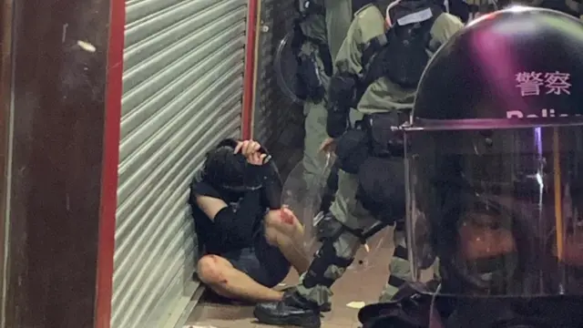 A man cowers against a wall as police surround him