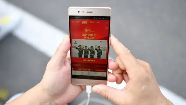 A man looks at his phone while watching the military parade in Tiananmen Square, Beijing