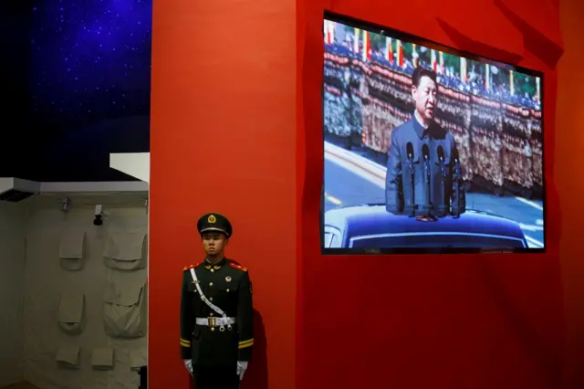 A paramilitary police officer stands guard next to a screen showing President Xi Jinping