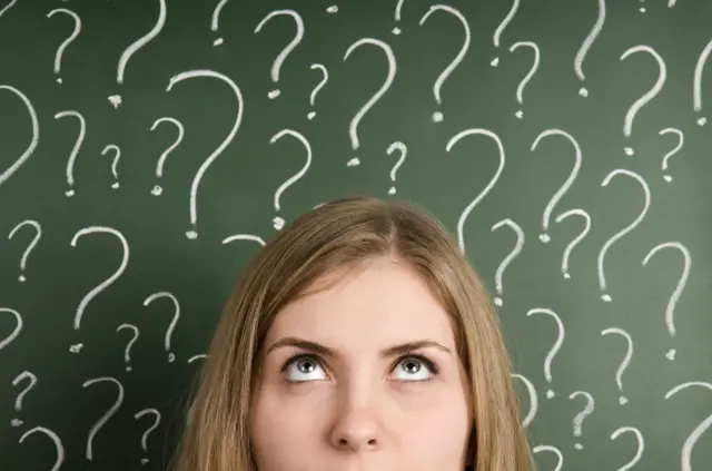 Chalk question marks above woman at blackboard