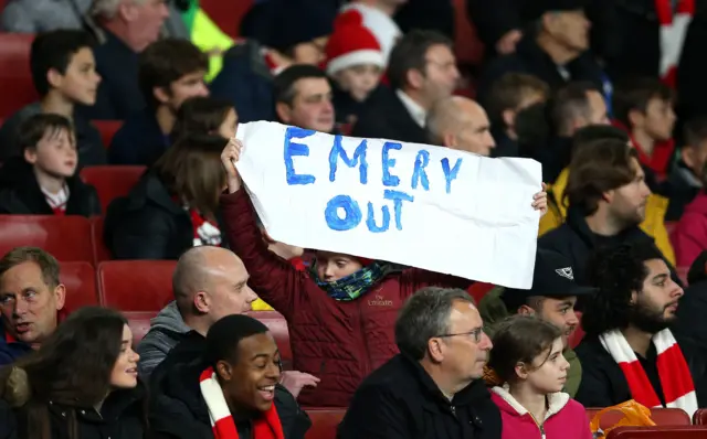 A young Arsenal fan holds up a banner in the stands reading "Emery Out" during the UEFA Europa League group F match at the Emirates Stadium