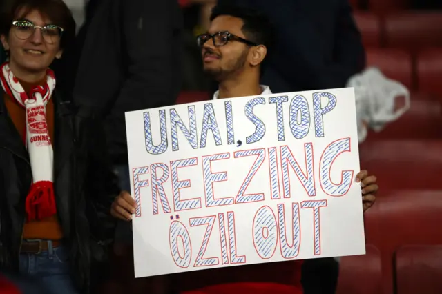 A fan holds a sign regarding Unai Emery and Mesut Ozil during the UEFA Europa League group F match between Arsenal FC and Vitoria Guimaraes at Emirates Stadium