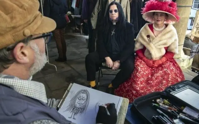 Two costumed Goths sit for a caricature drawing in Whitby