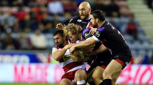 Ben Flower of Wigan Warriors is tackled by Gil Dudson and Tyrone McCarthy of Salford Red Devils