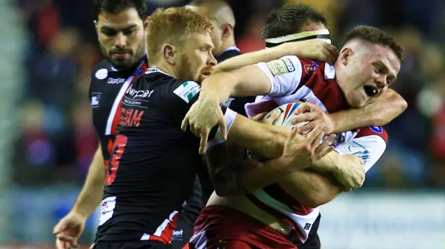 Joe Burgess of Wigan Warriors is tackled by Kris Welham of Salford Red Devils