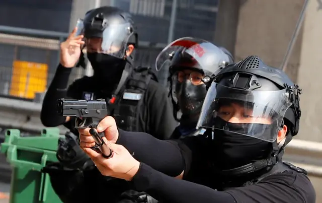 A riot police officer points a gun at protesters