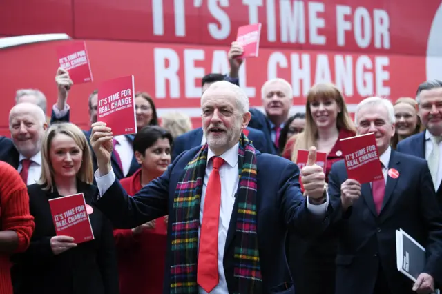 Britain"s Opposition Labour Party leader Jeremy Corbyn (C) poses as he arrives for the launch of his party"s manifesto in Birmingham