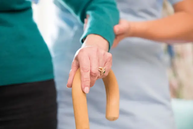 Elderly person being helped with walking stick