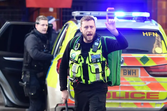 A medical officer gestures in front of an emergency vehicle