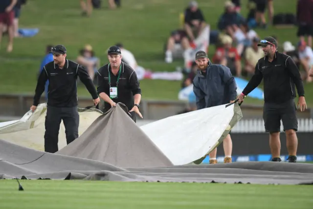 Ground staff pull the cover as the match is delayed due to rain