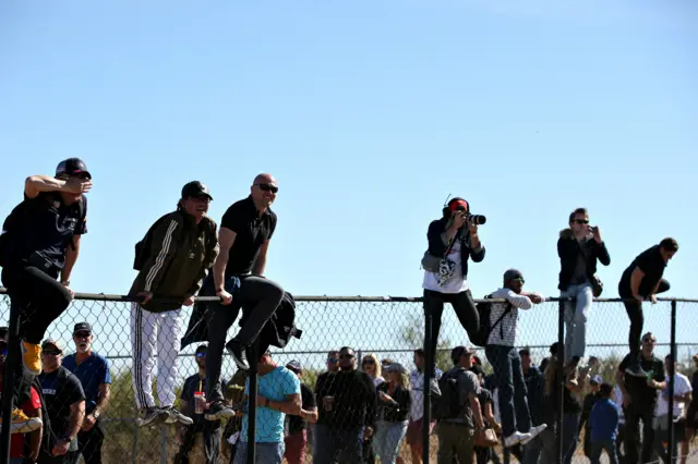 Fans perch on top of a fence to get a better view