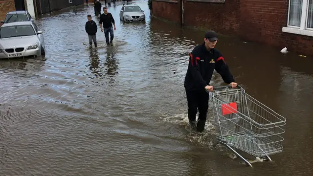 A person pushes a shopping trolley through water