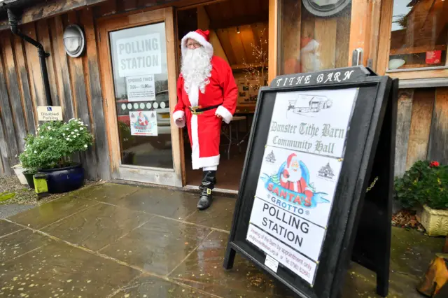 A man dressed as Father Christmas walks from his grotto at the Dunster Tithe Barn near Minehead, Somerset, which is being used as a polling station in the 2019 General Election.
