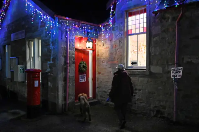 A man walks with a dog as he arrives to vote at a polling station in Furnace, near Inveraray