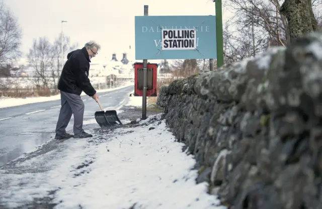 A man clears snow outside the Polling Station at the village hall in Dalwhinnie in the Cairngorms in the Highlands of Scotland.