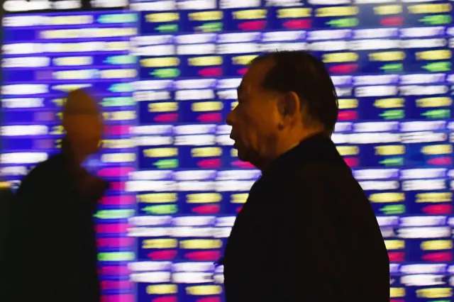 Men walk past stock market data board