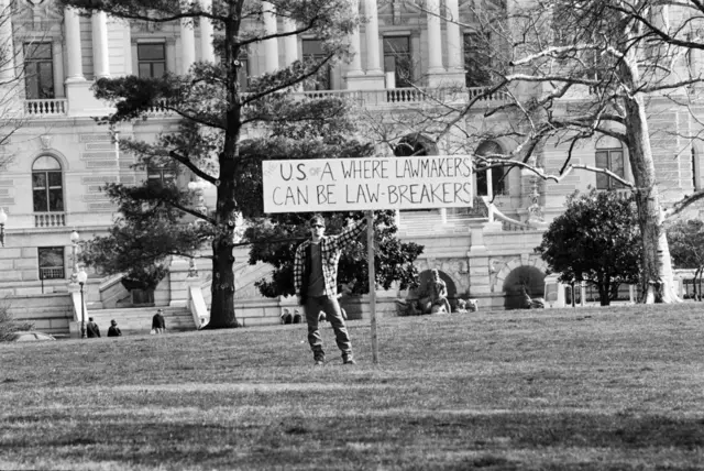 Protester holding sign: LAWMAKERS CAN BE LAW BREAKERS