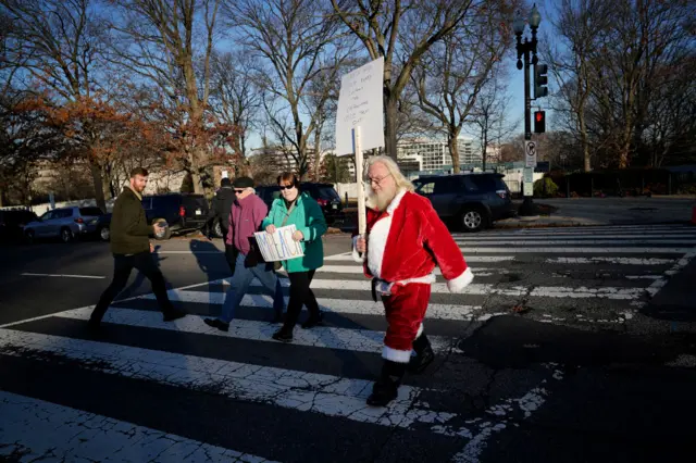 Tom McClain, dressed as Santa, holds a sign showing his support for President Trump