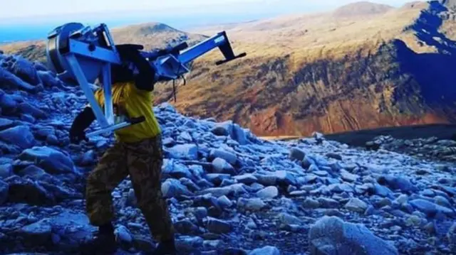 Man climbing mountain carrying rowing machine