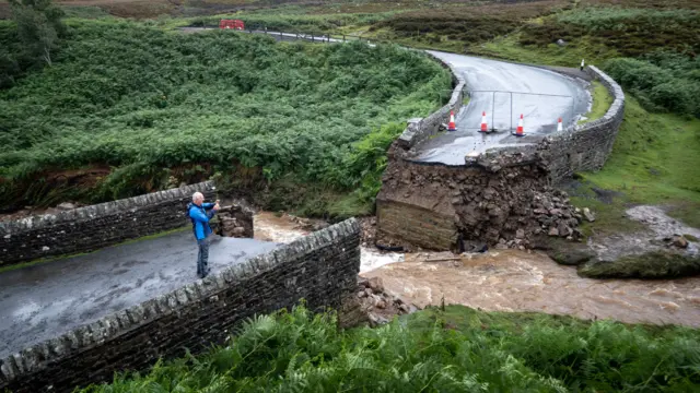 A man takes a photograph of a collapsed bridge near Grinton, North Yorkshire, after parts of the region had up to 82.2mm of rain in 24 hours on Tuesday.