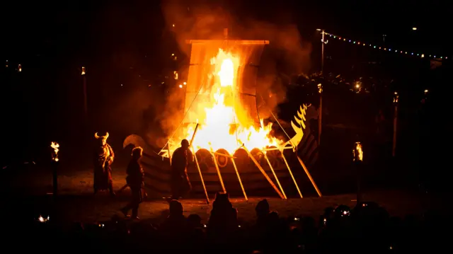 People in Viking costumes in front of a burning Viking boat during the Flamborough Fire Festival