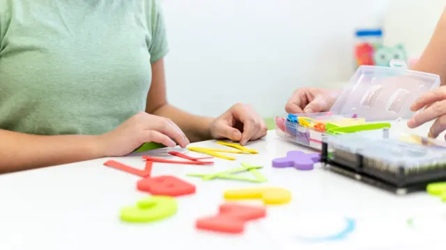 Therapist helping teenage girl with learning difficulties during child therapy. Top view hand detail of a therapist with patient. - stock photo