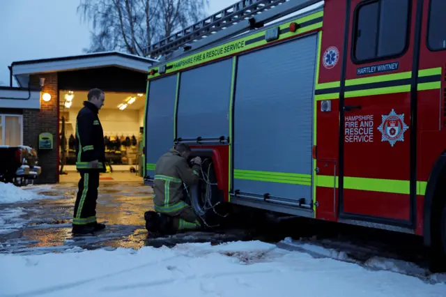 Retained firefighters fit snow chains to the tyres of the appliance outside the fire station in Hartley Wintney, in Hampshire,