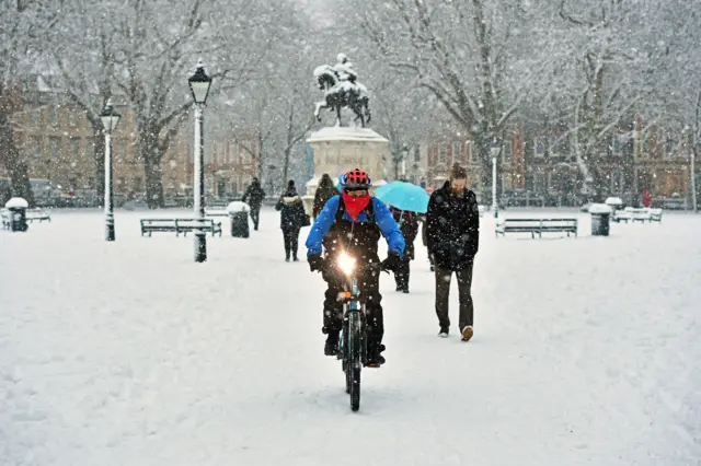 A cyclist rides through Queen Square in Bristol after snowfalls yesterday and overnight were expected to bring widespread disruption