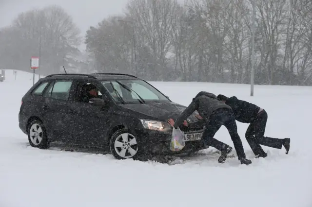 Two men help a driver try to get his car moving, after snowfalls yesterday and overnight have brought widespread disruption