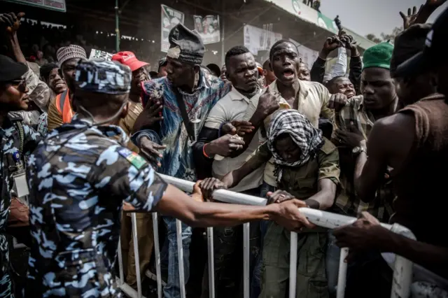 Supporters of the Nigerian opposition Peoples Democratic Party (PDP) presidential candidate push barriers in front of security forces during their candidate"s final campaign rally on February 14, 2019, at Ribadu Square in Jimeta, Adamawa State, eastern Nigeria