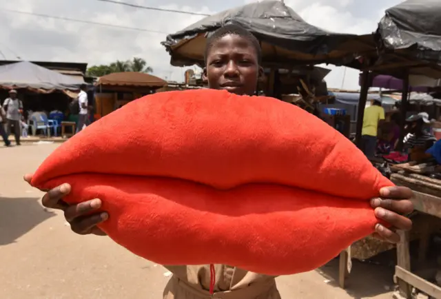 A boy poses with a pillow shaped like lips on sale for Valentine's Day in Yopougon, a suburb of Abidjan, on February 13, 2018