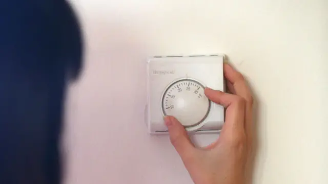 A woman uses a thermostat