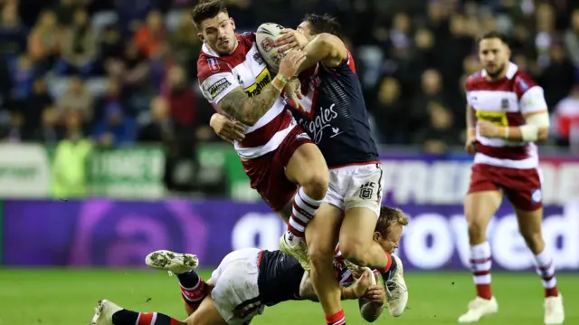 Oliver Gildart of Wigan Warriors is tackled by Jake Friend and Luke Keary of Sydney Roosters