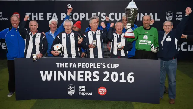 Eight men in their football kit pose for a photo with a winner's cup