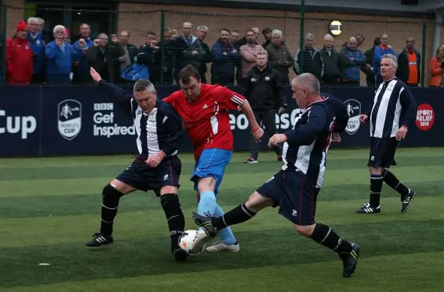 players on the pitch playing a game of 5-a-side football while a crowd look on behind the barriers