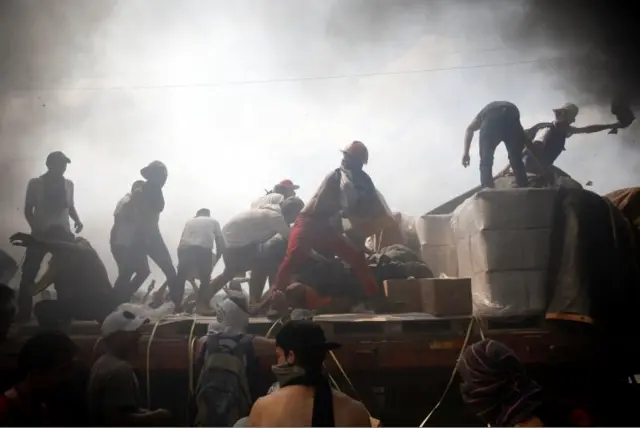 Opposition supporters unload humanitarian aid from a truck that was set on fire after clashes with Venezuelan security forces