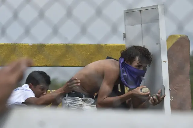 Also at the Simón Bolívar bridge, a demonstrator takes shelter behind an improvised shield