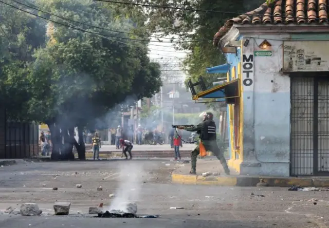 A member of Venezuela's security forces aims his shotgun while clashing with demonstrators in Urena, Venezuela