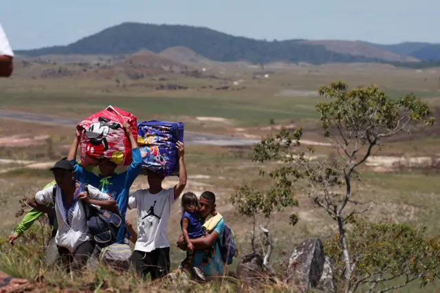 People walk with their belongings through a field, as they try to cross the border between Venezuela and Brazil in Pacaraima, Roraima