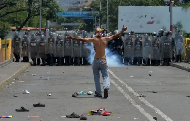 A demonstrator gestures in front of Venezuelan national police standing guard at the Simón Bolívar International Bridge