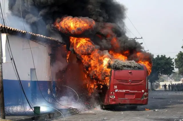 A bus is set on fire by demonstrators as security forces take their positions in Urena