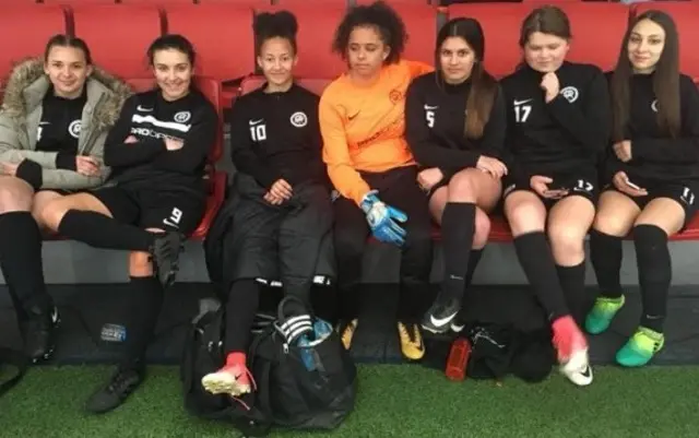 A team of young FA Peoples Cup female players sit in a row in their football kit