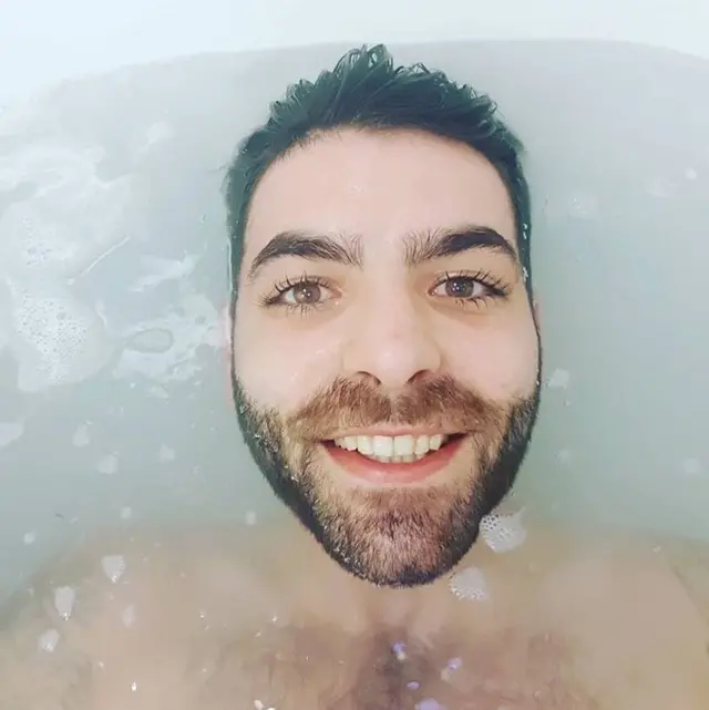 close up photo of a mans face smiling to camera while he's lying in a bath