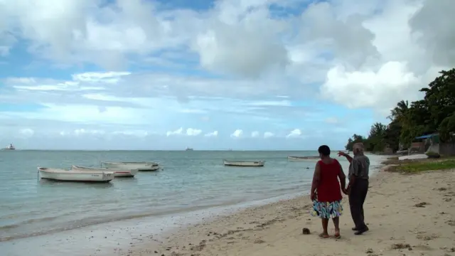 A couple stand on a beach on the Chagos Islands, facing out to sea.