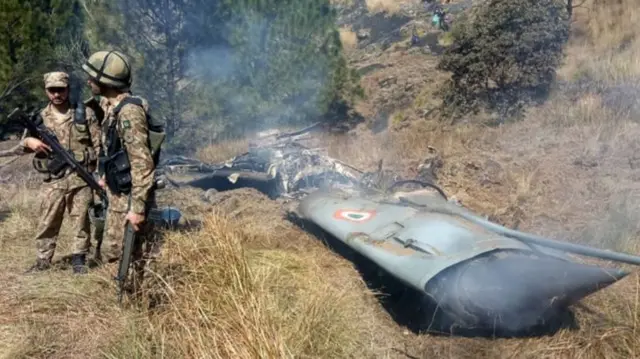 Pakistani soldiers stand next to what Islamabad says is the wreckage of an Indian fighter jet shot down in Pakistan-run Kashmir