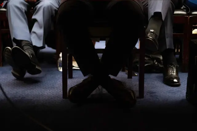 Cohen's legs are crossed under the desk