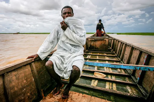 A man partially covers his face with his tunic as travels on a boat on drought-stricken Lake Chad.