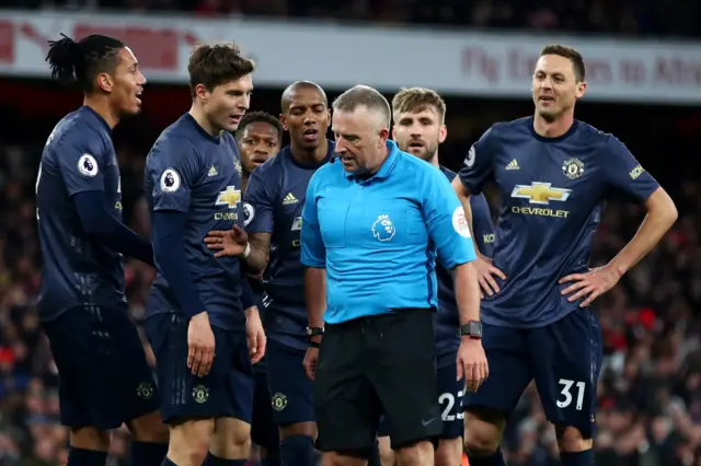 Referee Jon Moss is surrounded by the Man Utd players