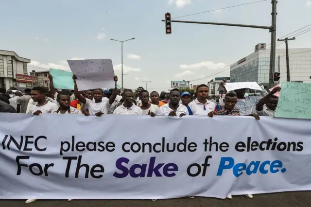 Protesters hold a banner reading 'Please conclude the elections for the sake of peace' during a demonstration against the suspension of governorship elections in Port Harcourt, Rivers State