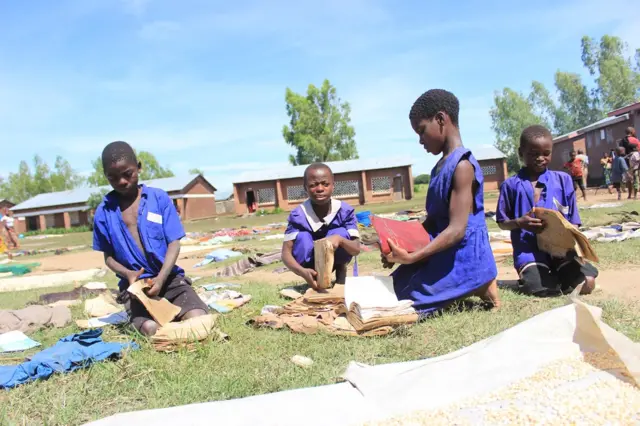 Children attempt to dry out their school books after they were caught in the floods